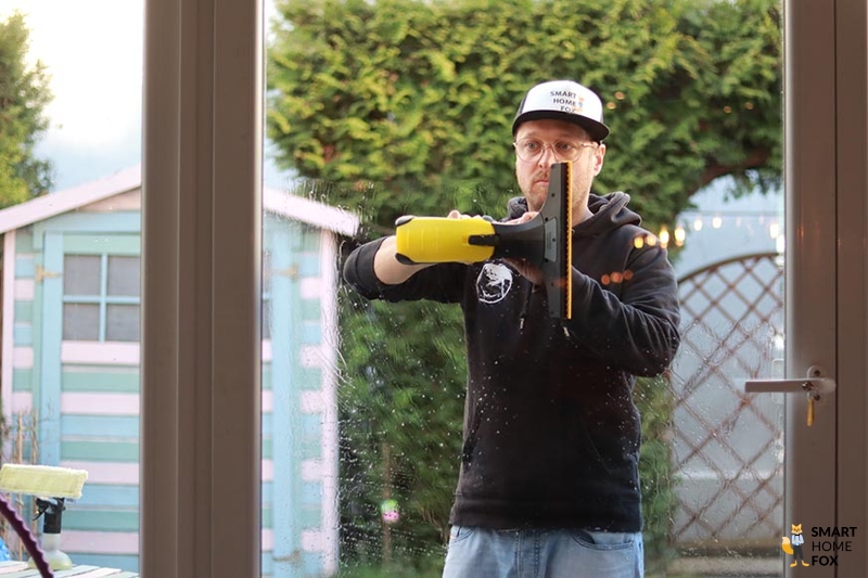 Man sieht wie ein Mann ein Fenster absaugt mit dem Fenstersauger.